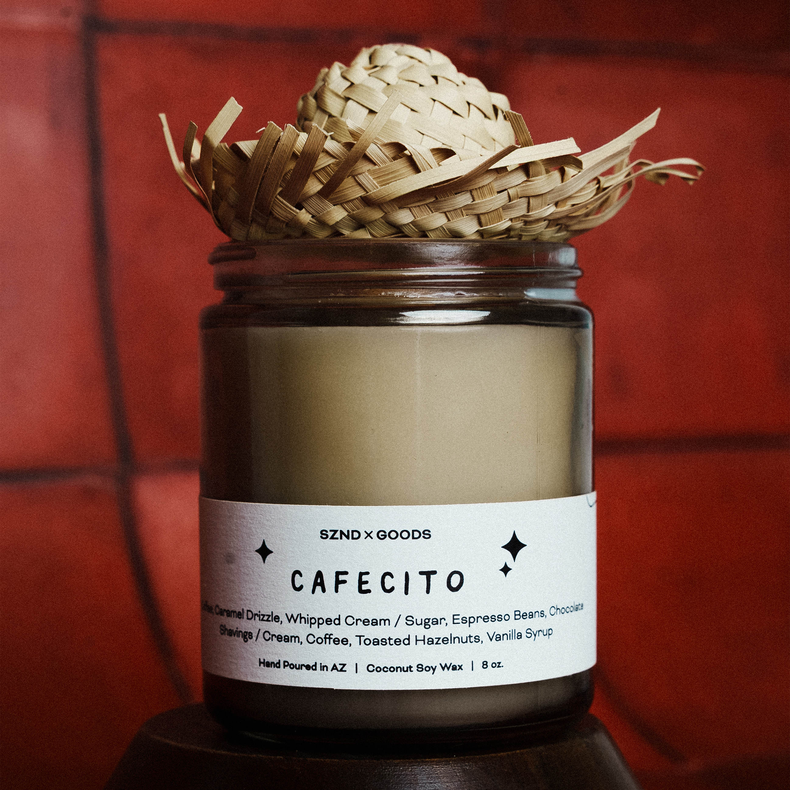 Candle labeled 'CAFECITO' with a wicker basket on top against a red tiled wall.