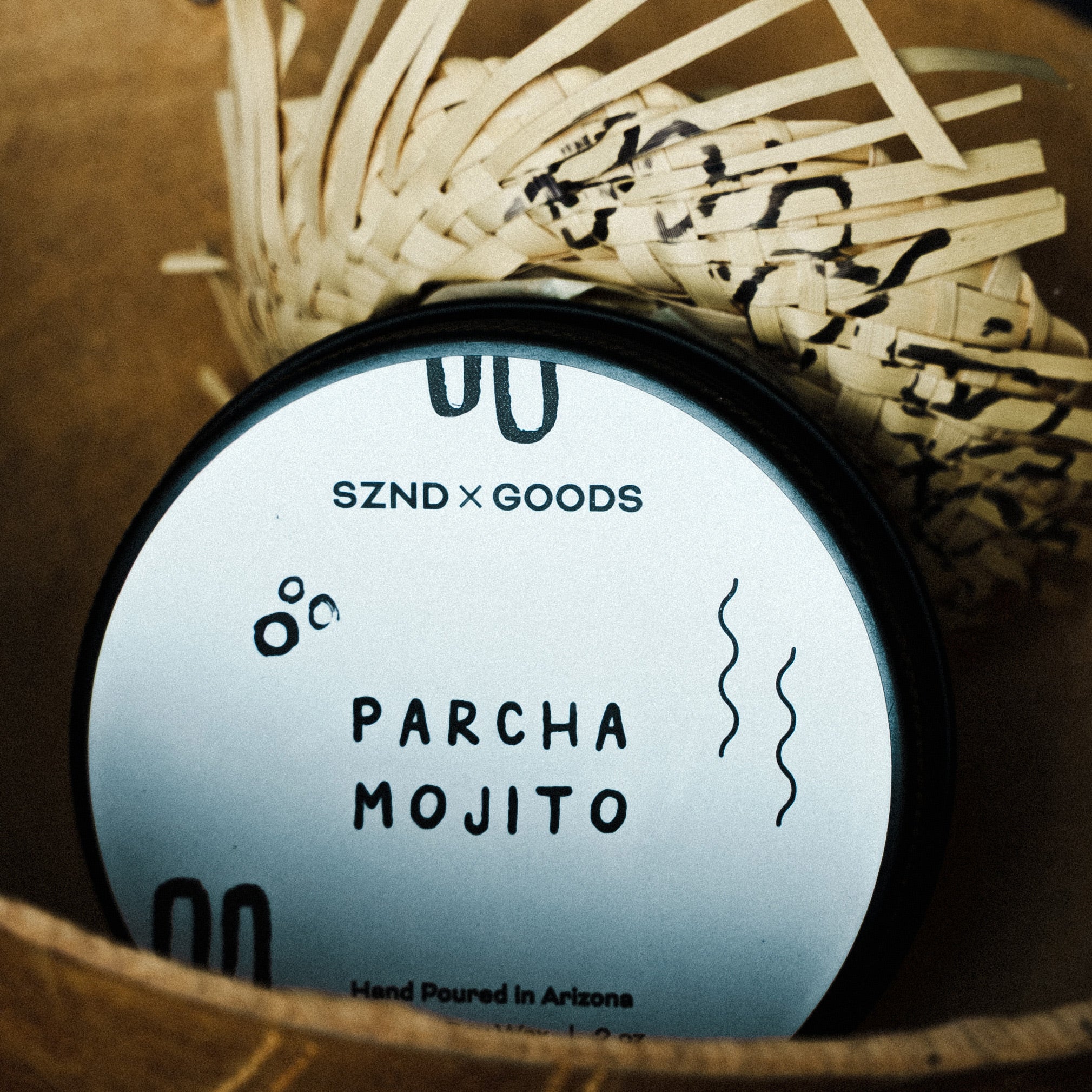 Mini 2oz candle container labeled 'Parcha Mojito' by SZND GOODS with wicker basket in the background.