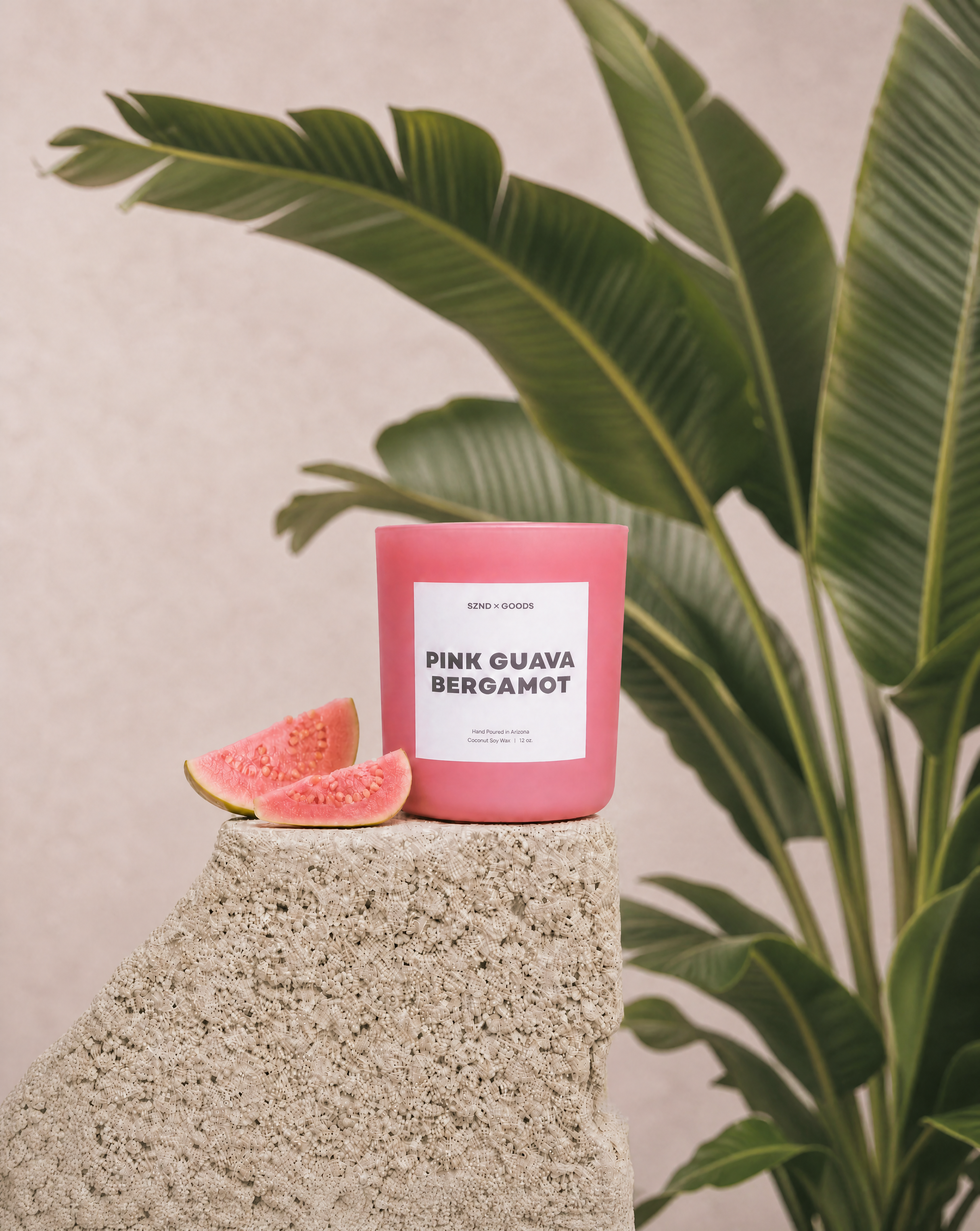 Pink candle labeled 'Pink Guava Bergamot' on a stone surface with a plant in the background