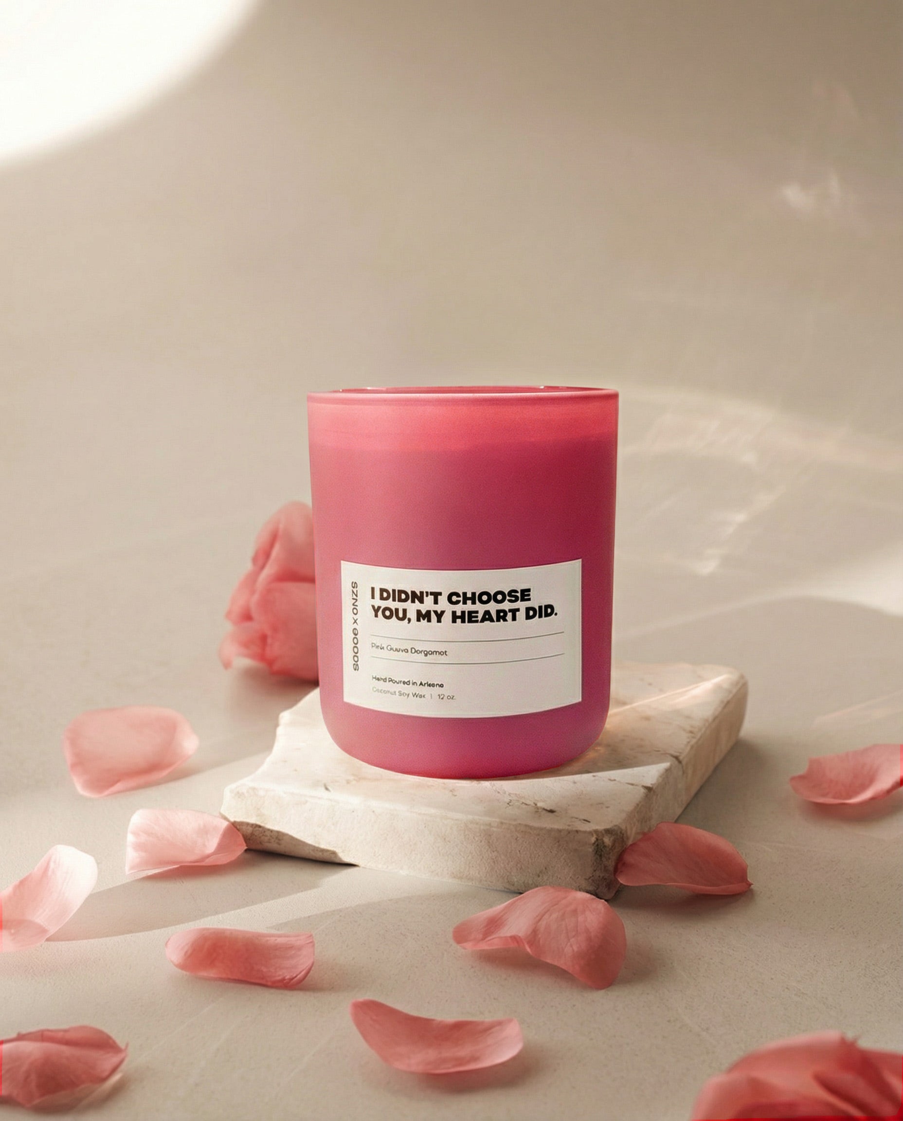 Pink candle with a white label on a stone surface with pink petals around.