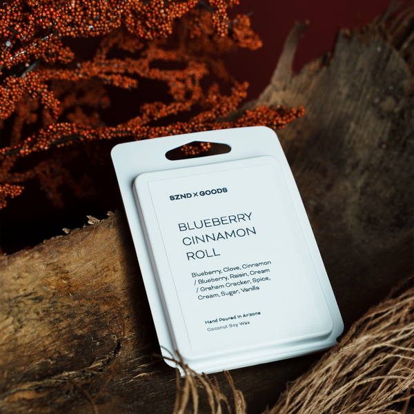 Scented wax melt packaging labeled 'Blueberry Cinnamon Roll' on a rustic background.