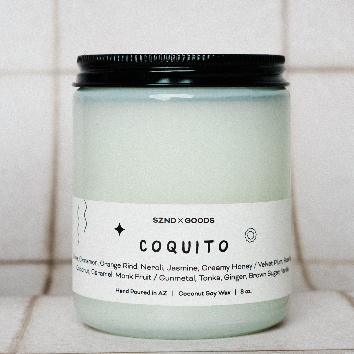 8oz Candle jar labeled 'Coquito' with a black lid on a tiled surface