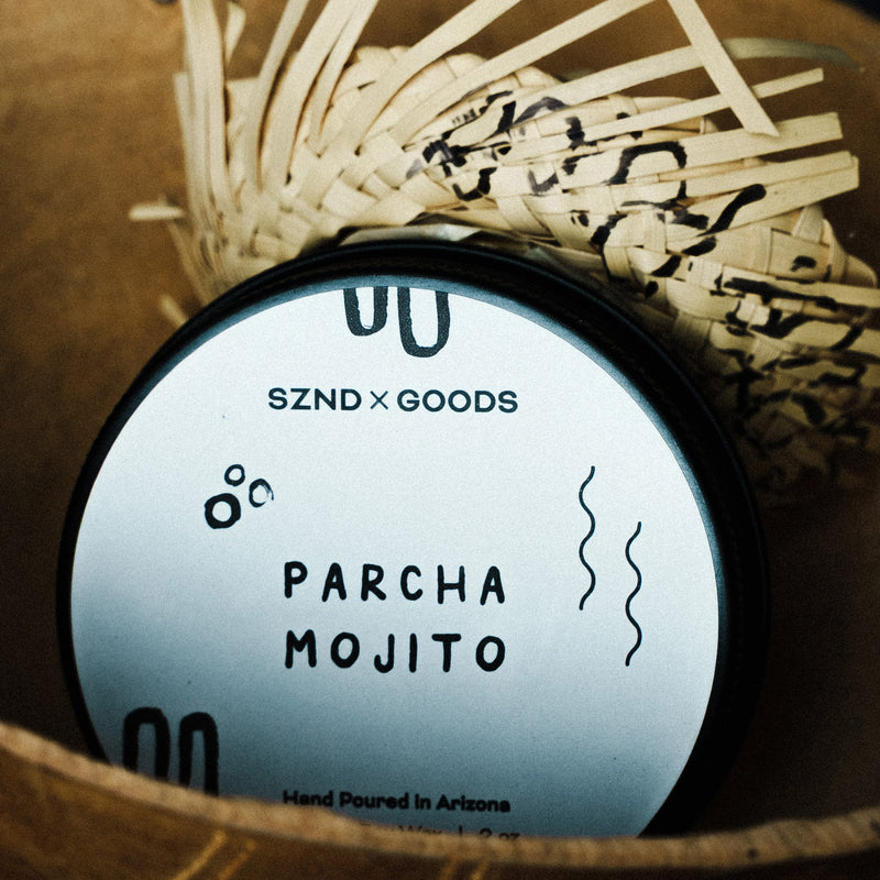 Mini 2oz candle container labeled 'Parcha Mojito' by SZND GOODS with wicker basket in the background.