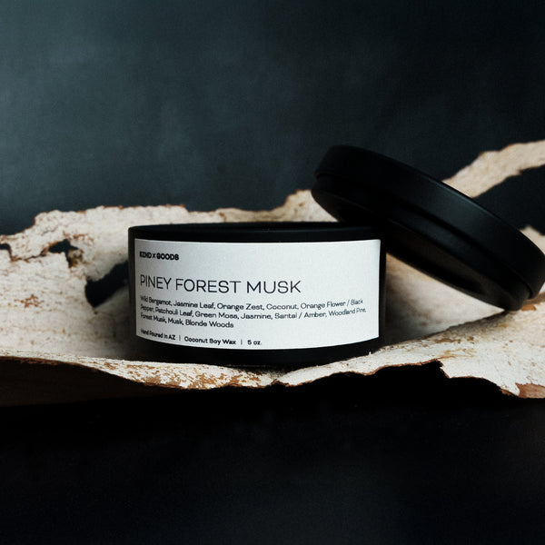 Candle labeled 'Piney Forest Musk' on a dark background