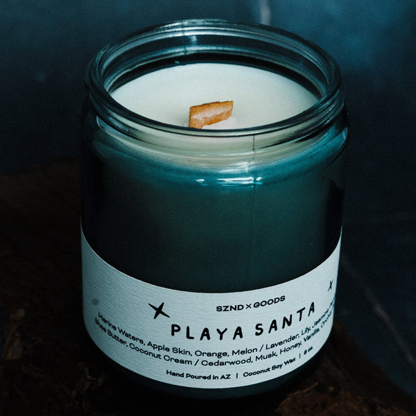Candle in a glass jar labeled 'Playa Santa' with a dark background