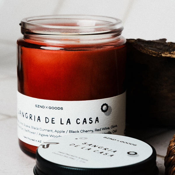 Sangria de la Casa candle in a glass jar with a label on a neutral background with a mini 2oz candle.