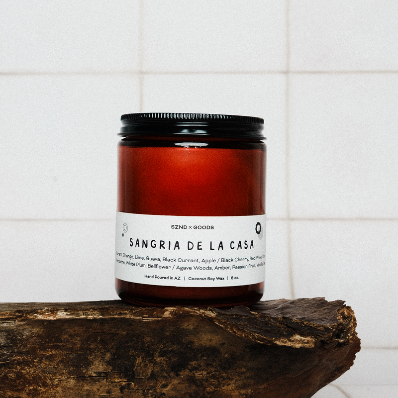 Sangria de la Casa wooden wick candle on a wooden surface with a white tiled background.