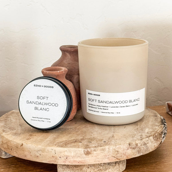 12oz and 2oz beige candle and container labeled 'Soft Sandalwood Blanc' on a stone surface.