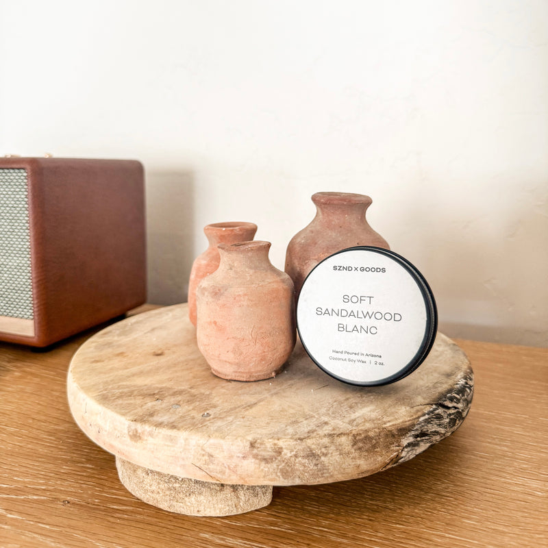 2oz travel candle and vases on a wooden surface with a speaker in the background