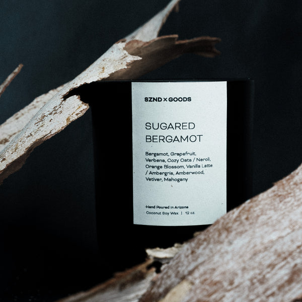 Scented candle labeled 'Sugared Bergamot' by SZND x GOODS on a dark background with natural elements.