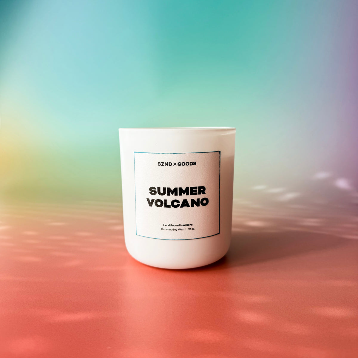 A white candle with a wooden lid labeled 'SUMMER VOLCANO' on a dual-tone background with blue at the top and pink at the bottom.