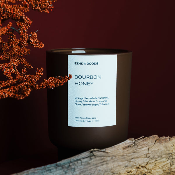 Candle labeled 'Bourbon Honey' by SZND x GOODS with decorative elements on a dark background