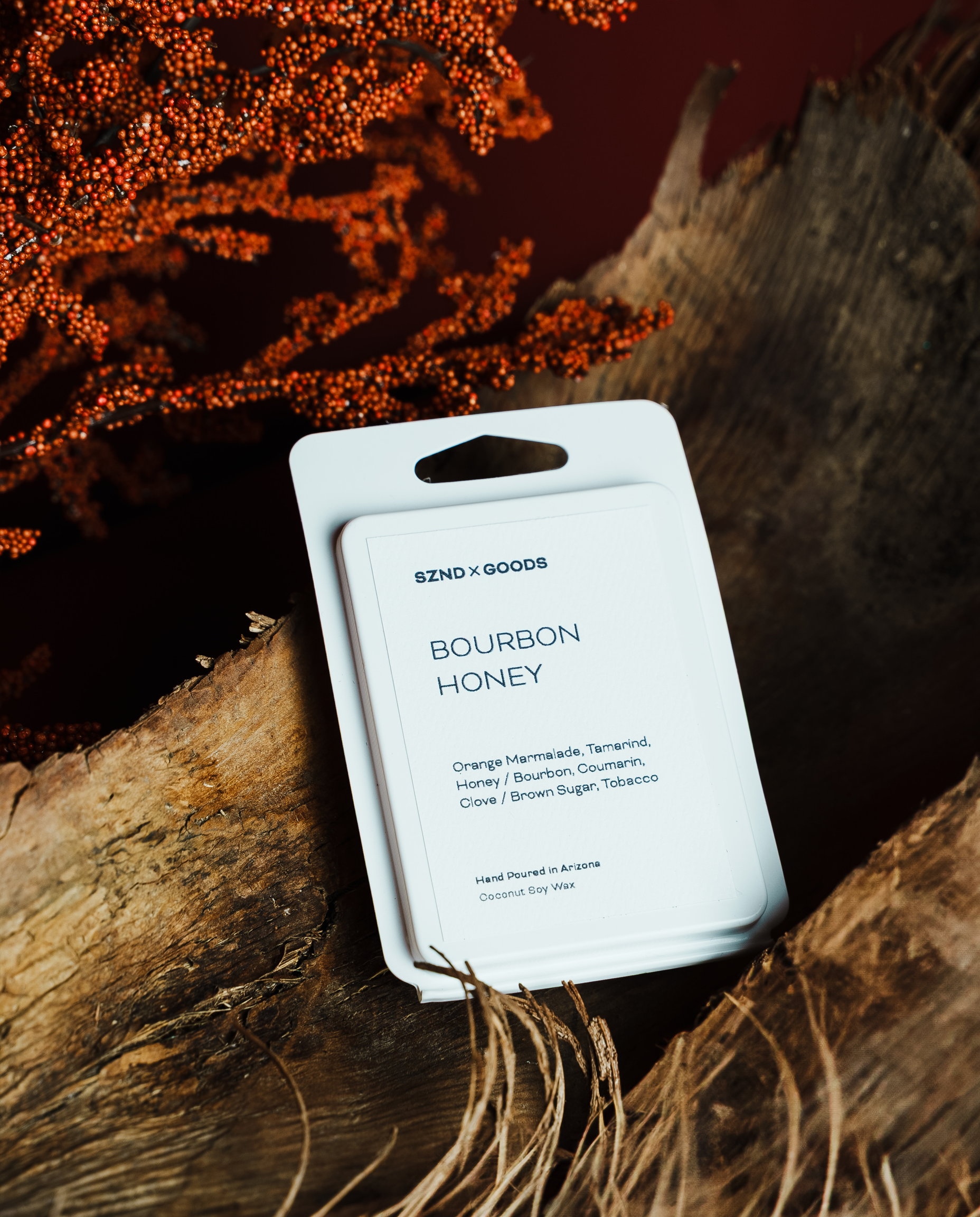 Bourbon Honey wax melt rests on a rustic piece of wood with dried grass and orange berries in the background.
