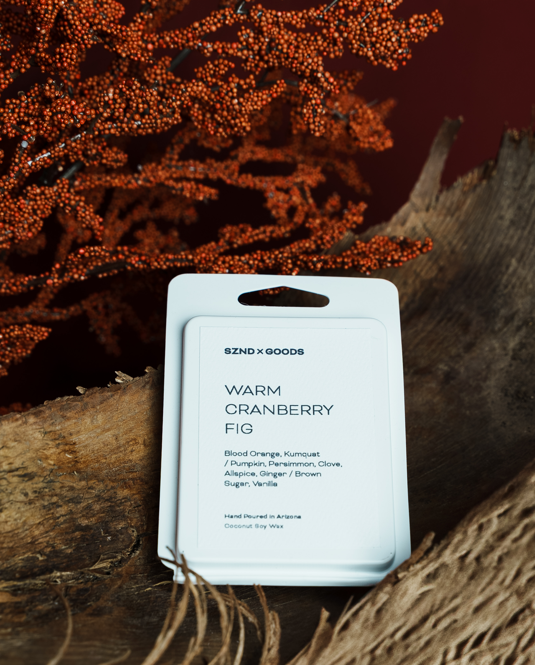 A Warm Cranberry Fig wax melt placed on a rustic wood surface with dried orange cranberry branches in the background.