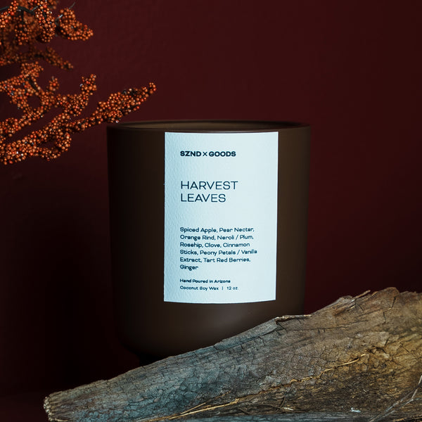 Candle labeled 'Harvest Leaves' by SZNDS Goods with decorative elements on a dark background