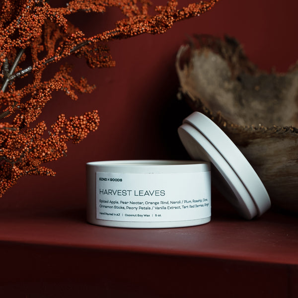 White candle container labeled 'Harvest Leaves' on a dark surface with decorative elements.