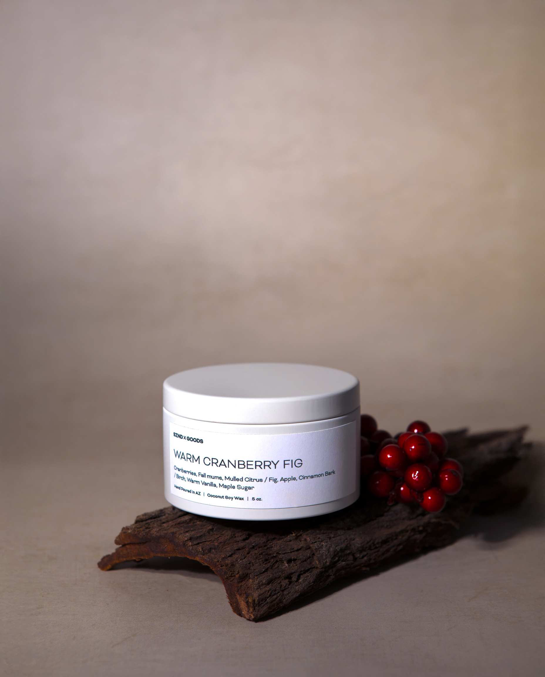 The 5oz Warm Cranberry Fig candle styled on a piece of wood with cranberries.